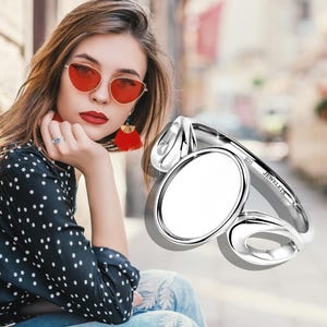 Può includere: Un anello d'argento con un centro ovale e due disegni curvi aperti. L'anello è contrassegnato con "925 JEWELETS". È un gioiello.