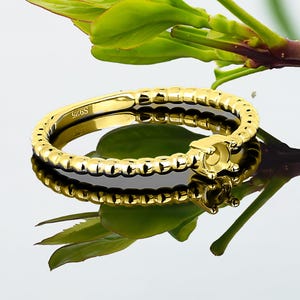 Op de afbeelding: Een gouden ring met een getextureerde band en een klauwbevestiging voor een edelsteen. De ring is gemarkeerd met "925S" aan de binnenkant.