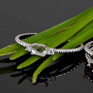 May include: A silver ring with an oval-shaped setting and three small round stones. The ring is on a bed of green grass.