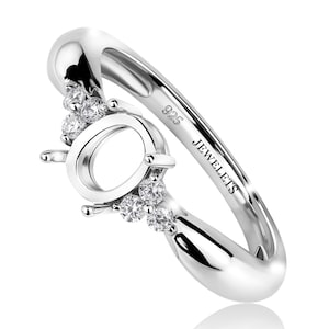 Può includere: Un anello in argento lucido con un gruppo di piccole gemme scintillanti. L'anello presenta un design aperto unico con il testo "JEWELETS" e "925" inciso sulla fascia. L'anello è progettato per contenere una pietra centrale.