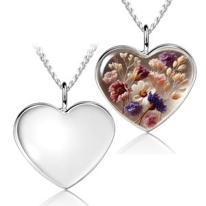 May include: Two heart-shaped pendants on silver chains. One pendant is solid silver, the other is clear with dried flowers in shades of pink, purple, and white. The pendants are displayed on a white background.