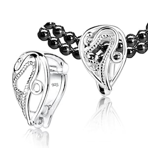 May include: Two silver earrings with a teardrop design. Each earring has an openwork pattern with a central, textured element. The earrings are marked with "925". A black beaded necklace is visible in the background.