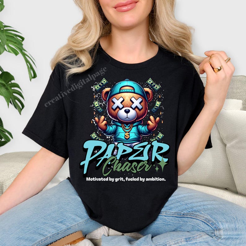 Może przedstawiać: Czarny t-shirt z kresk&oacute;wkowym misiem w niebieskiej czapce i bluzie z kapturem, z symbolami dolara i napisem "PAPER CHASER". Miś ma X na każdym oku. Tekst "Motywowany odwagą, napędzany ambicją" znajduje się poniżej.