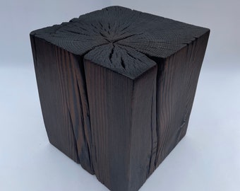 May include: A dark brown wooden cube stool with a natural wood grain pattern. The stool is made of reclaimed wood and has a rustic, industrial look.