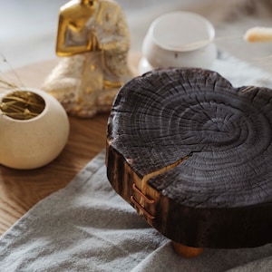 Puede incluir: Una mesa redonda de madera oscura con un borde natural y detalles en cobre. La mesa está sobre un paño de lino gris. Una estatua dorada de Buda está en el fondo.
