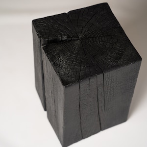 Può includere: Un cubo di legno nero con evidenti motivi a venature. Il cubo è realizzato in legno massello e ha un aspetto rustico e naturale.