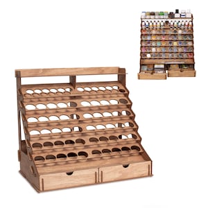 May include: A wooden paint bottle organizer with multiple tiers and circular openings for holding bottles. The organizer has two small drawers at the bottom and a top shelf. The word "PLYWOOD" is visible on the top of the organizer.