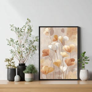 Könnte beinhalten: Ein gerahmter Kunstdruck mit abstrakten Blumen in Orange-, Weiß- und Gelbtönen vor einem beigen Hintergrund. Das Kunstwerk wird auf einer Holzoberfläche mit dekorativen Pflanzen in schwarzen und weißen Töpfen ausgestellt.