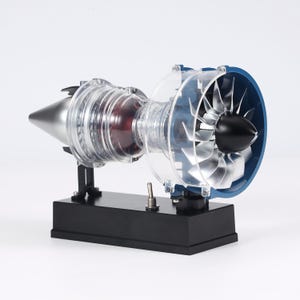 May include: A detailed model of a jet engine, showcasing internal components. The engine features a silver nose cone, transparent casing, and a blue and black fan assembly. It is mounted on a black base with a switch.