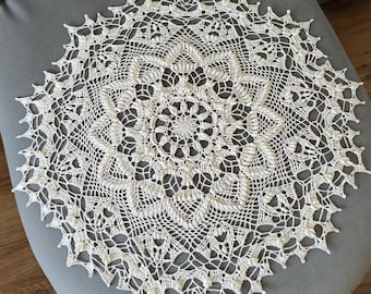 May include: A white crocheted doily with a delicate, intricate design. The doily is circular and has a centre with a starburst pattern.