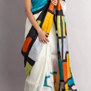 Pode incluir: Um sari sem mangas com base branca e um padrão geométrico arrojado em preto, amarelo, turquesa, laranja e verde-limão. O design consiste em grandes formas irregulares coloridas, delimitadas por linhas pretas espessas.