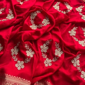 May include: Red silk saree with a gold border and intricate floral embroidery. The embroidery features white beads and sequins.
