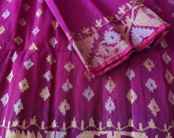 May include: A vibrant magenta textile with a repeating diamond pattern. The fabric features a decorative border with gold and silver geometric designs. The folded section reveals a detailed edge, showcasing the intricate craftsmanship of the textile.