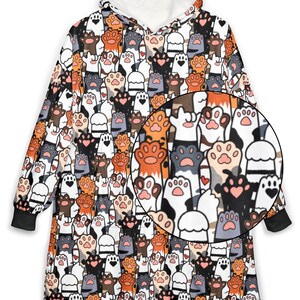 May include: A hooded blanket featuring a repeating pattern of cat paws in various colors, including orange, black, gray, and white. The interior hood and trim are white, and the cuffs are black. The blanket is designed for comfort and warmth.
