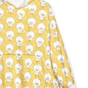 K&ouml;nnte beinhalten: Gelbe Kapuzen-Decke mit einem sich wiederholenden Muster aus wei&szlig;en Cartoon-Enten. Die Kapuze und die Manschetten sind wei&szlig;, und die Decke hat eine K&auml;ngurutasche. Die Enten haben orangefarbene Schn&auml;bel und F&uuml;&szlig;e.