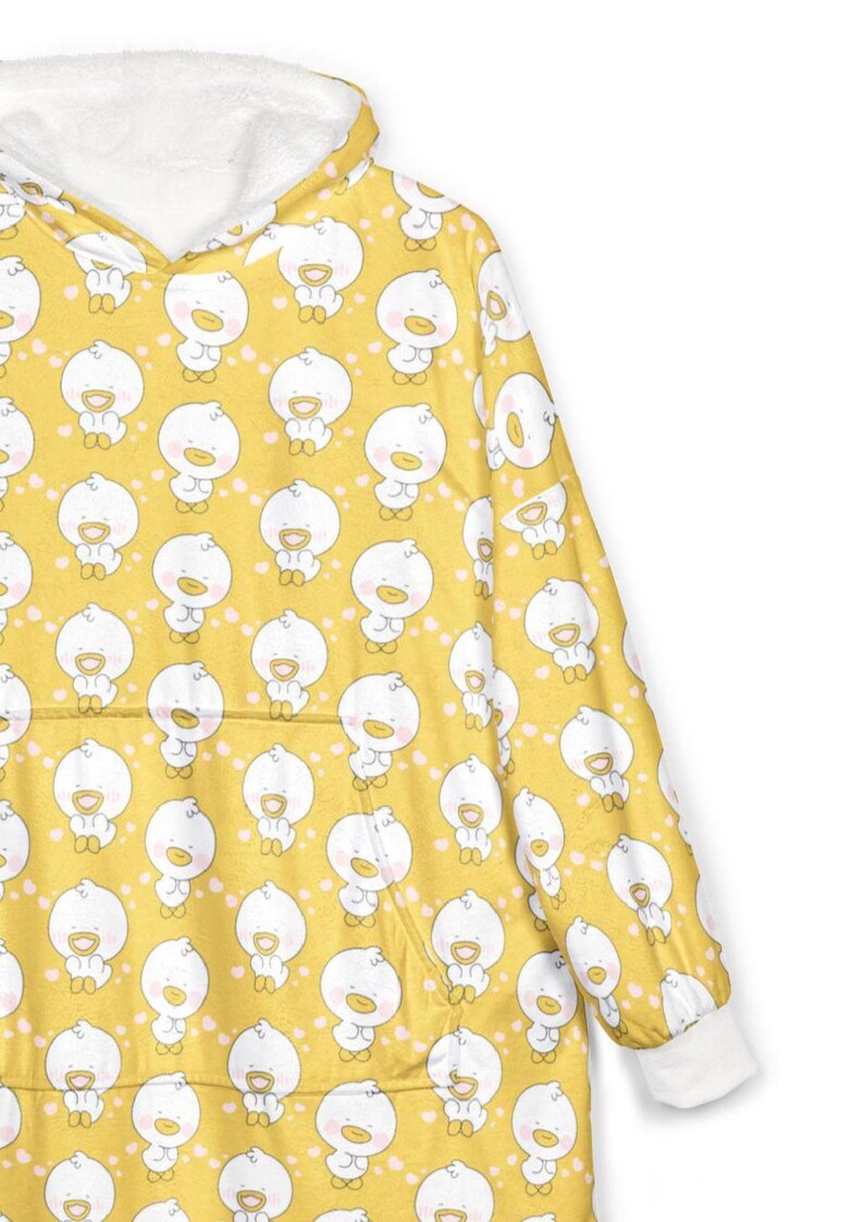 K&ouml;nnte beinhalten: Gelbe Kapuzen-Decke mit einem sich wiederholenden Muster aus wei&szlig;en Cartoon-Enten. Die Kapuze und die Manschetten sind wei&szlig;, und die Decke hat eine K&auml;ngurutasche. Die Enten haben orangefarbene Schn&auml;bel und F&uuml;&szlig;e.