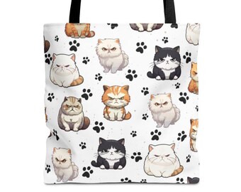 May include: White tote bag featuring a repeating pattern of cartoon cats in various colors, including orange, black, and white. The cats have grumpy expressions and are interspersed with black paw prints. The bag has black handles.