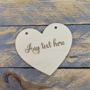 May include: A wooden heart-shaped sign with holes for hanging. The sign is blank and has the text "Any text here" engraved on it.