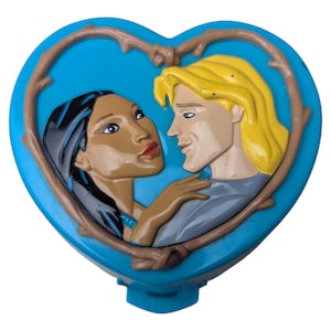 May include: A blue heart-shaped compact with a relief of two figures framed by brown vines. The figures are a woman with black hair and a man with blonde hair, facing each other. The compact has a small blue clasp at the bottom.