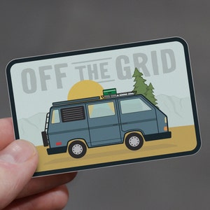 May include: A sticker with a blue van with a roof rack and a green box on top. The van is driving on a yellow road with a green tree and a yellow sun in the background. The text "OFF THE GRID" is at the top of the sticker.