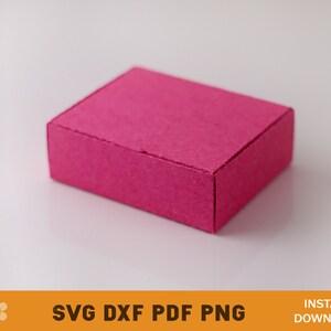 Puede incluir: Una peque&ntilde;a caja rectangular de color rosa hecha de cart&oacute;n. La caja tiene una superficie texturizada y est&aacute; sobre un fondo blanco.