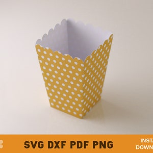 Puede incluir: Una caja de papel amarilla y blanca con lunares y un borde festoneado. La caja est&aacute; vac&iacute;a y est&aacute; sobre una superficie blanca.