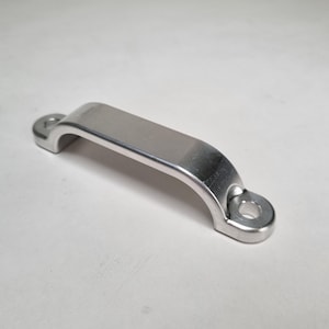 May include: A shiny, silver-colored metal handle with a curved design. The handle has a flat, rectangular center section and rounded ends with circular holes for mounting. The object is likely a cabinet or drawer pull.