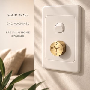 Puede incluir: Una placa de interruptor de pared blanca con una perilla de control de ventilador circular de latón macizo mecanizado por CNC. La perilla muestra un icono de ventilador central con ajustes 0, I, II y III. El texto dice SOLID BRASS, CNC MACHINED, PREMIUM HOME UPGRADE.