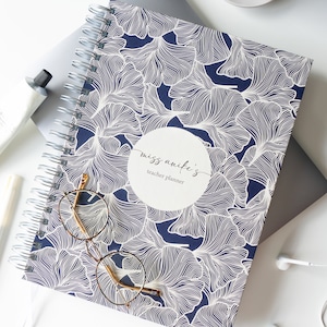 May include: A blue spiral bound teacher planner with a white ginkgo leaf pattern. The cover has a white circle with the text "miss anife's teacher planner".