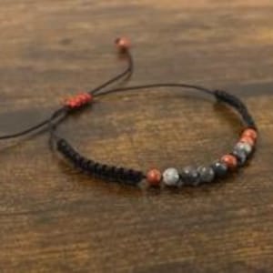 May include: A black cord bracelet with red and gray stone beads.