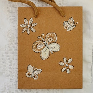 Piccola borsa regalo, decorata a mano con farfalle e fiori, su carta kraft riciclata.