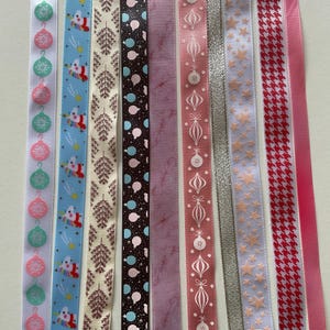 Puede incluir: Una colección de cintas decorativas con varios diseños y colores. Las cintas presentan patrones como adornos navideños, Papá Noel, estrellas y pata de gallo. Los colores incluyen blanco, azul, rosa, marrón y rojo. Ideal para envolver regalos y manualidades.