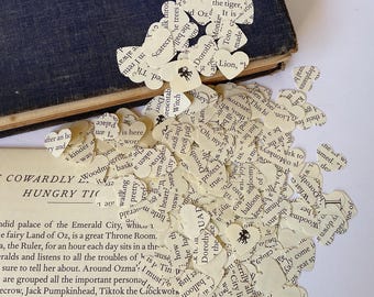 May include: A collection of heart-shaped paper cutouts scattered around an open book. The hearts are made from book pages, with visible text. The book is open to a page with text from "The Cowardly Lion of Oz".