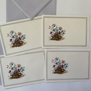 May include: Stationery set featuring cream-colored cards with a floral design in the corner. The flowers are in shades of purple, blue, and white, with green foliage. Each card has a gray border. A gray envelope is also included.