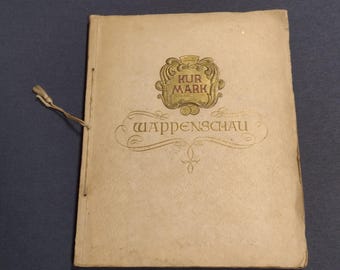 Puede incluir: Un libro de color beige con un emblema dorado en la portada. El emblema tiene las palabras "Kur Mark" en letras rojas. El título del libro es "Wappenschau" en letras doradas.