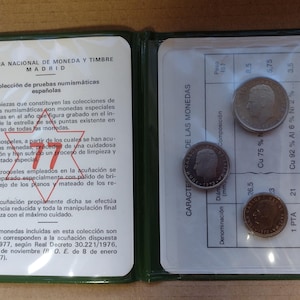 Peut inclure: Un classeur vert de collection de pièces de monnaie avec du texte en espagnol et trois pièces exposées. Les pièces sont en argent et en bronze, avec des portraits et du texte détaillés. Le classeur est ouvert, montrant les pièces et le texte descriptif.