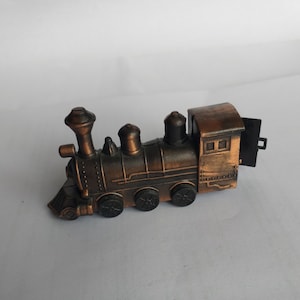 May include: A vintage-style metal toy train with a brown and black finish. The train has a large engine with a smokestack and several smaller cars.