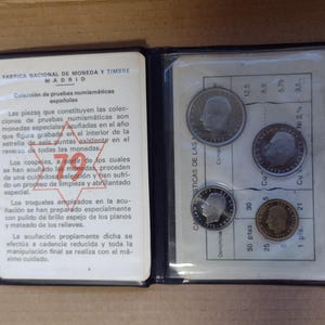 Peut inclure: Un album de collection de pièces de monnaie noir, ouvert pour montrer plusieurs pièces dans des pochettes en plastique transparent. L'album contient du texte en espagnol. Les pièces ont divers motifs et dénominations.