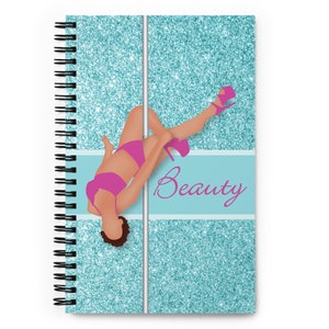 Könnte beinhalten: Ein spiralgebundenes Notizbuch mit einem türkisfarbenen Glitzerumschlag. Der Umschlag zeigt eine Silhouette einer Frau in einem rosafarbenen Outfit, auf dem Kopf stehend, die sich an einer silbernen Stange festhält. Der Text "Beauty" ist in rosa Kursivschrift auf einem hellblauen Streifen geschrieben.