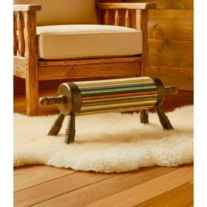 May include: A cylindrical footstool featuring a multi-colored striped fabric cover with horizontal bands of green, blue, yellow, and brown. The stool has dark brown wooden ends and four matching dark brown wooden legs with a turned spindle design.