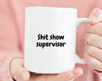 May include: White ceramic coffee mug with black text that reads "Shit show supervisor".