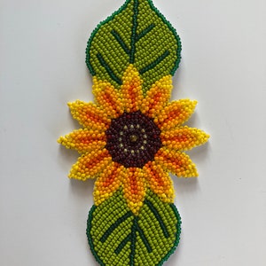 Può includere: Un girasole perlato con petali gialli, arancioni e rossi, un centro marrone e due foglie verdi.