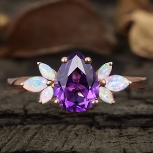 May include: A pear-shaped amethyst engagement ring set in rose gold with a halo of white opals.