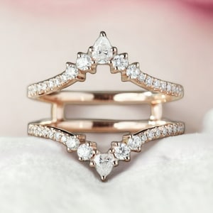 May include: A rose gold ring with a delicate, curved design. The ring is set with small diamonds and features a larger pear-shaped diamond at the center.