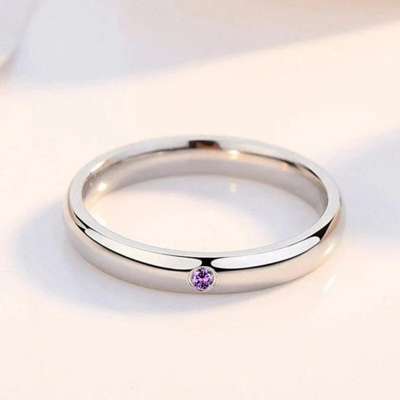 May include: A simple silver band ring with a small purple gemstone set in the center.