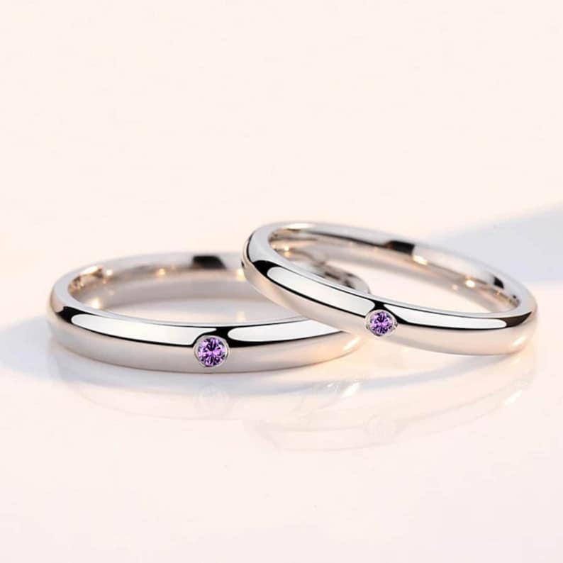 May include: Two silver wedding bands with a small purple gemstone set in each band.