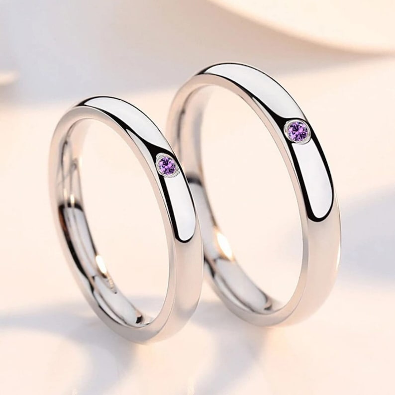 May include: Two silver wedding bands with a small purple gemstone on each.