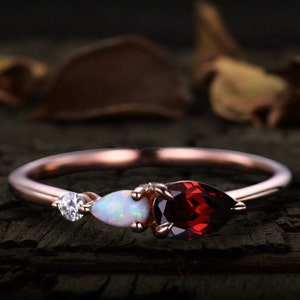 May include: A rose gold ring featuring a pear-shaped red garnet, a pear-shaped white opal, and a small round diamond.