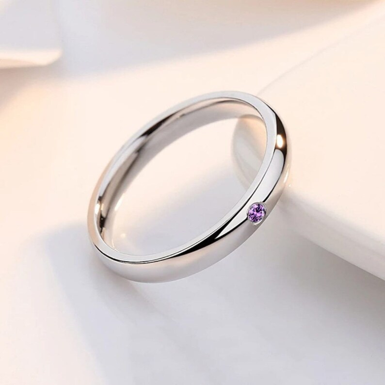 May include: A silver band ring with a small purple gemstone set in the center.