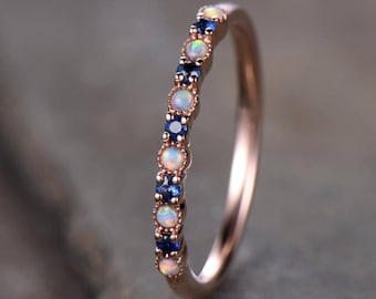 May include: A delicate rose gold band ring with alternating white opal and blue sapphire gemstones.